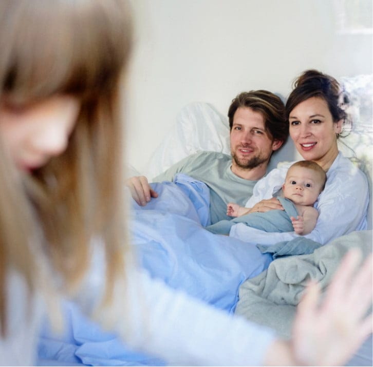 Spinale Muskelatrophie: Familie mit Neugeborenem im Bett